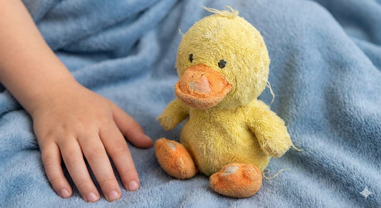 Plush yellow duck toy on a soft blue blanket beside a child's hand, Montessori-inspired play