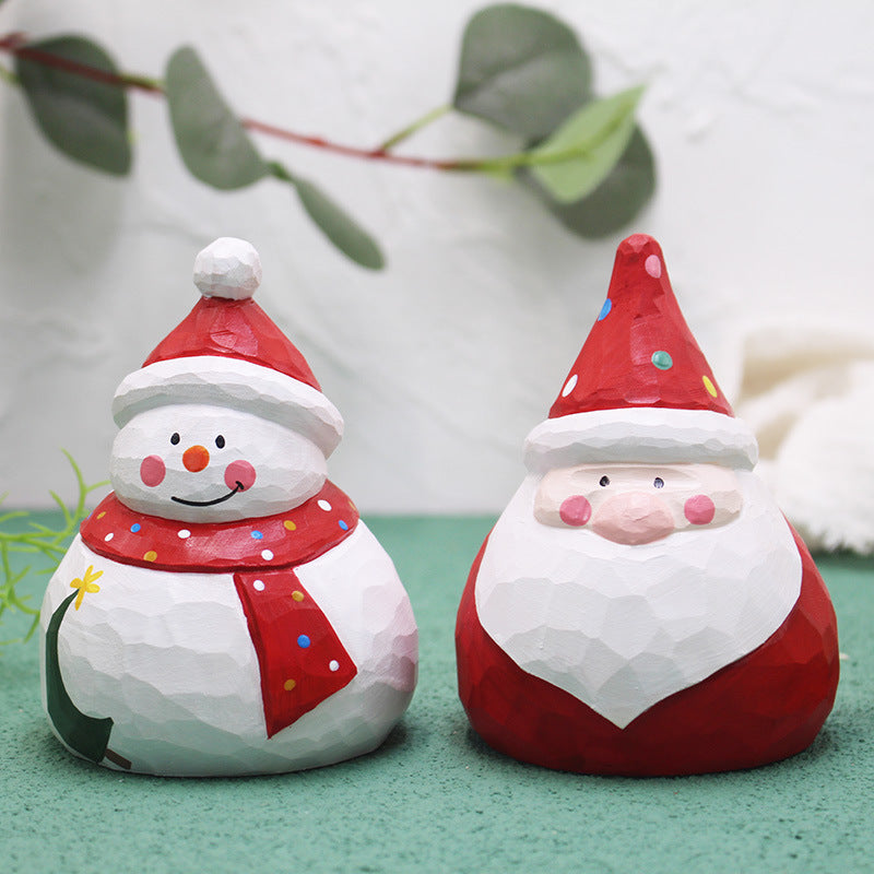 Two Christmas-themed figurines, one resembling a snowman and the other a Santa Claus, on a green surface with a blurred background.