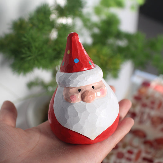 Hand holding a small Santa Claus figurine with a blurred green plant background