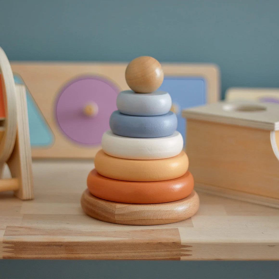 Stack of wooden rings in rainbow colors on a wooden surface with educational toys in the background.