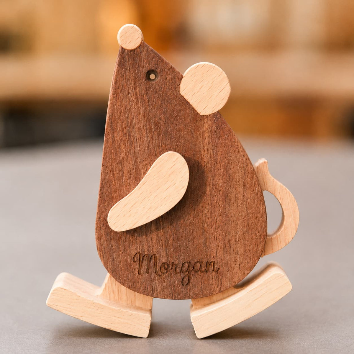 A personalized wooden mouse rocking toy with a medium brown body and light natural wood accents, featuring the name 'Morgan' engraved on the front, set against a blurred background.