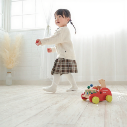 Toddler pulling Montessori wooden bear drum toy in bright, minimalist room