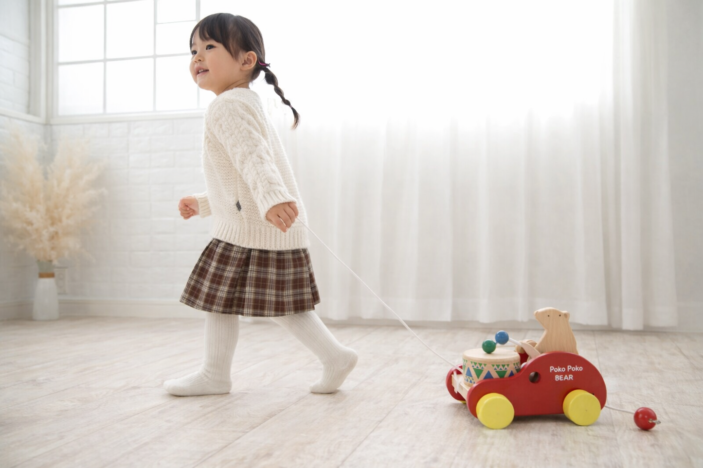 Toddler pulling handcrafted wooden bear drum pull toy in bright, airy room