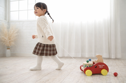 Toddler pulling handcrafted wooden bear drum pull toy in bright, airy room