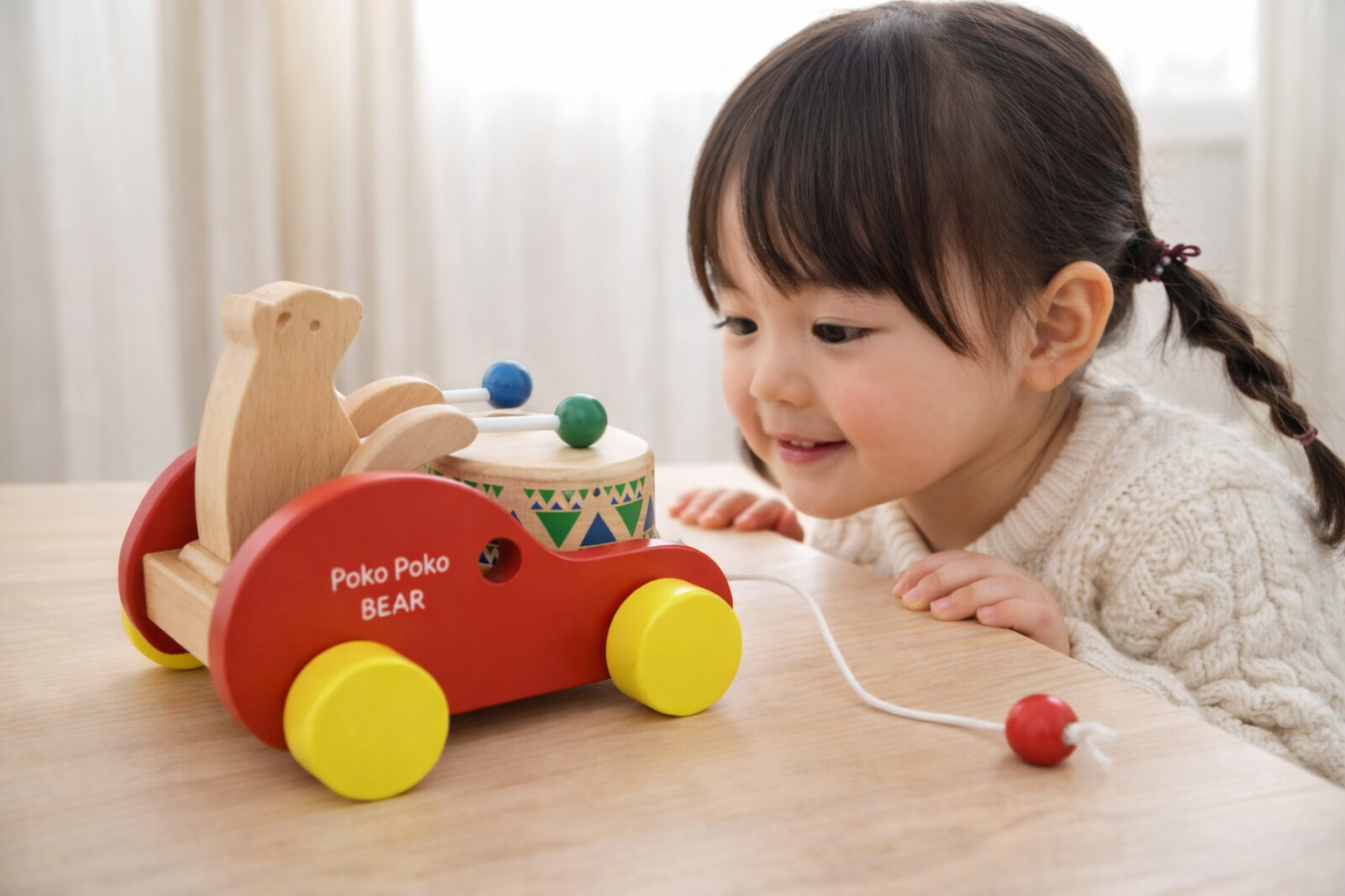 Toddler playing with handcrafted wooden bear drum pull toy on a table, Montessori style