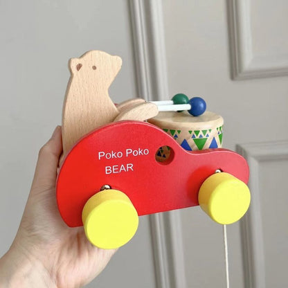 Hand holding a wooden bear drum pull toy with red body, yellow wheels, and Montessori design