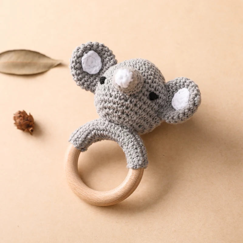 Crocheted mouse rattle toy with wooden ring on a beige background