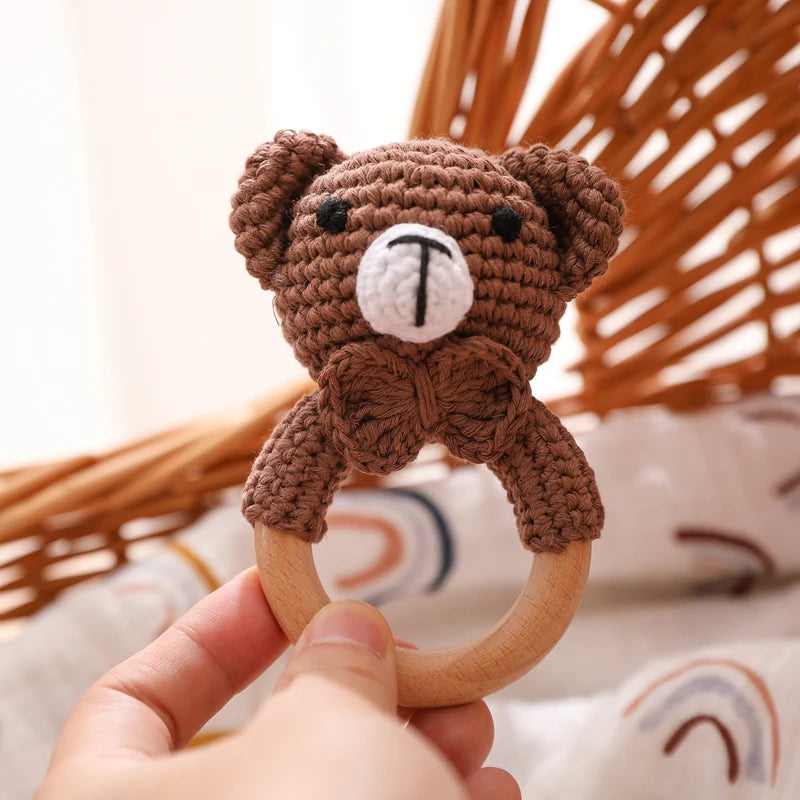 Hand holding a crochet teddy bear teething ring with a blurred background