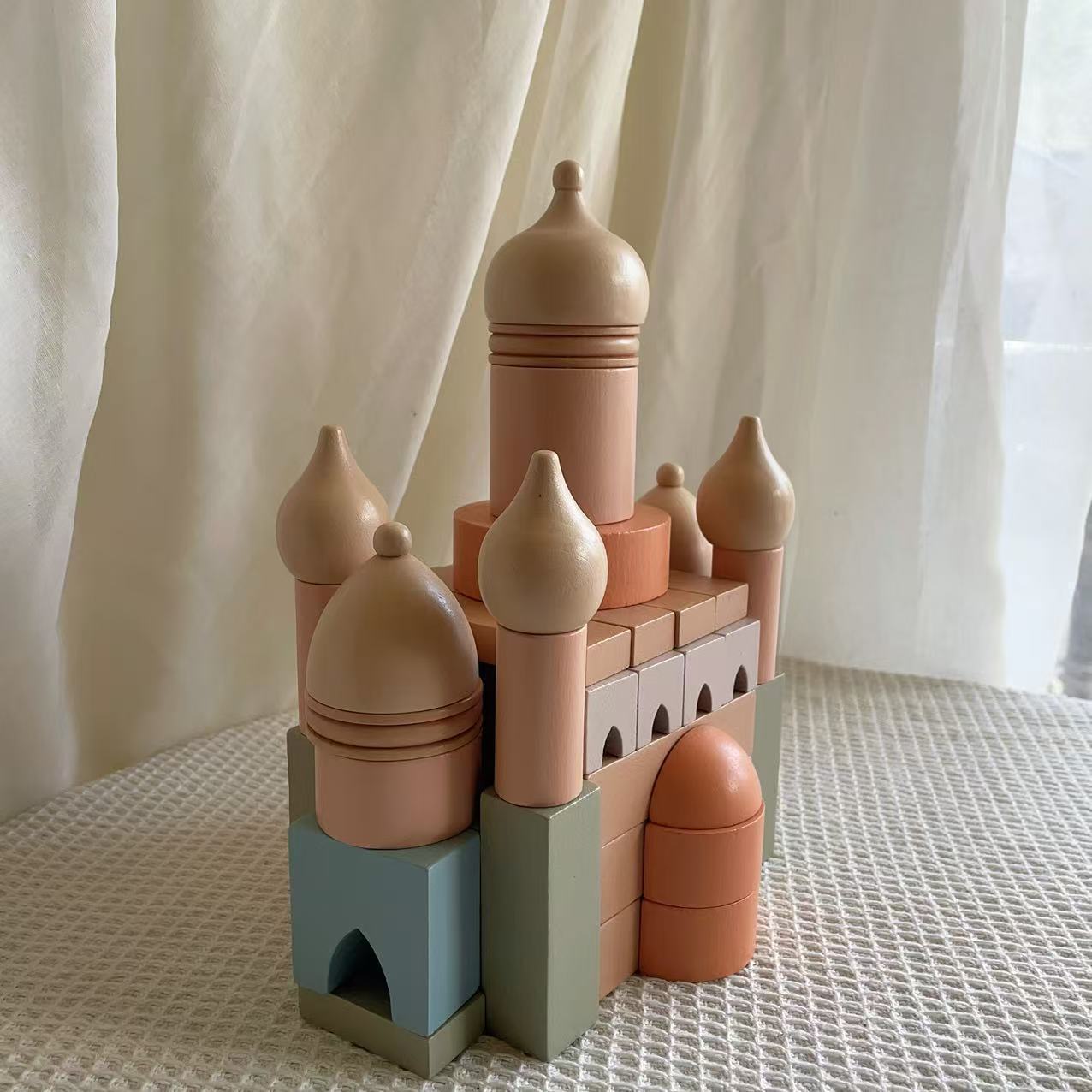 Toy castle made of interlocking blocks on a textured surface with a light curtain background