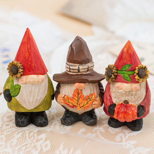 Three autumn-themed gnome figurines with colorful hats and leaf decorations on a lace tablecloth.