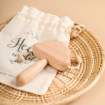Wooden baby rattle on a white cloth with a drawstring bag labeled 'Hello world' on a woven mat.