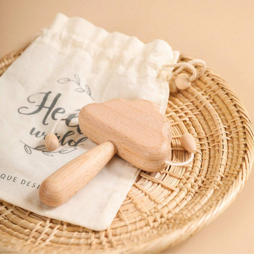 Wooden baby rattle on a white cloth with a drawstring bag labeled 'Hello world' on a woven mat.