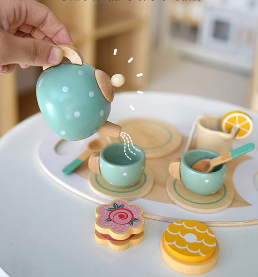 Wooden tea set with teapot, cups, and cookies on a white surface.