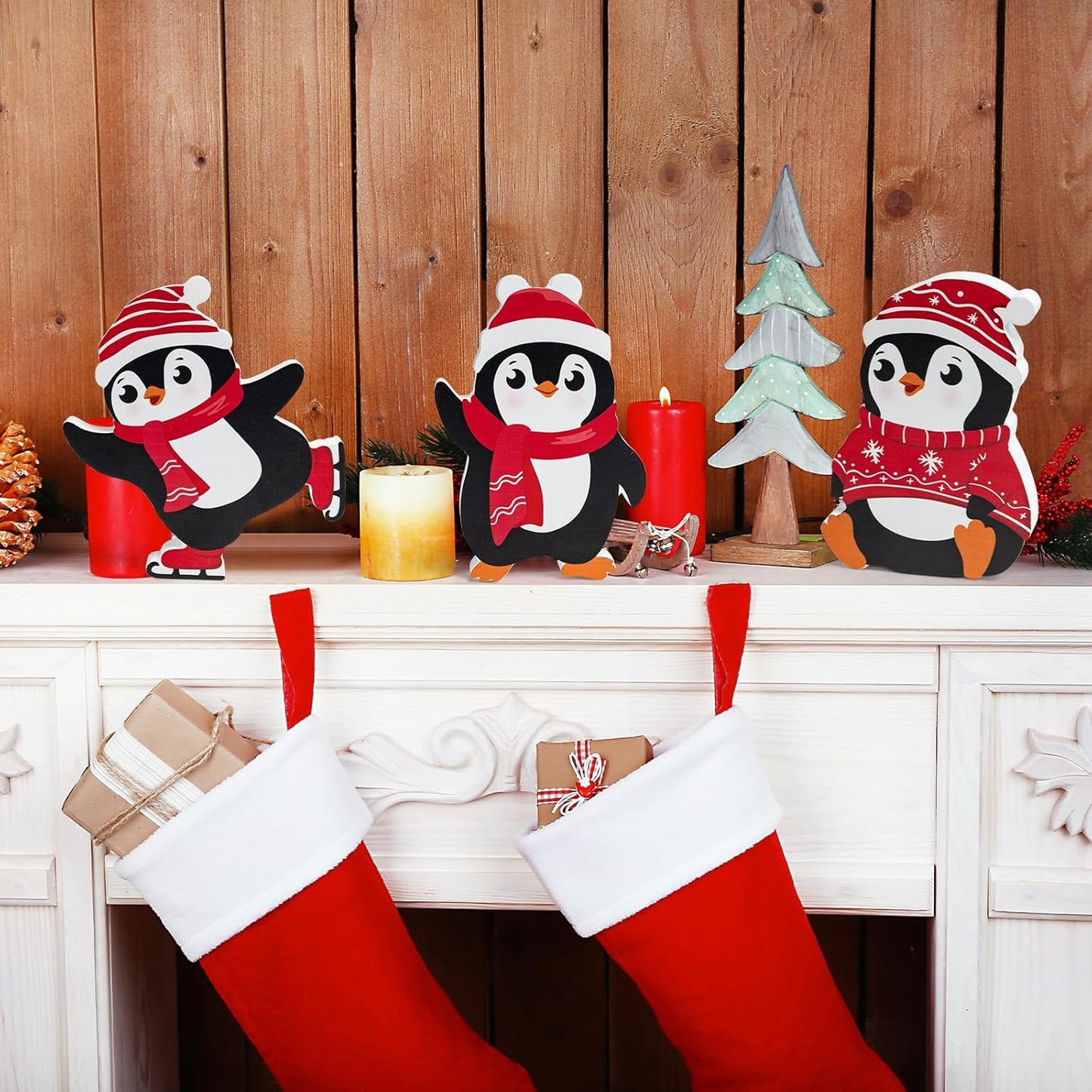 Decorative penguins with Christmas stockings and candles on a wooden mantel.