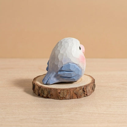 Back view blue and white wooden lovebird toy showing handpainted blue wings, geometric faceted bird figurine eco-friendly natural wood toy safe for toddlers on rustic wood slice
