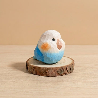 Handcrafted blue and white wooden lovebird toy with orange cheek, geometric low-poly design eco-friendly wooden bird figurine for toddlers on natural wood slice