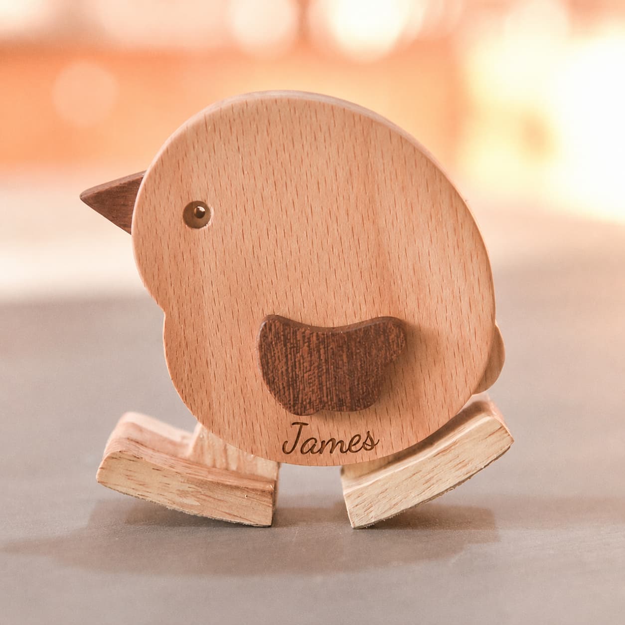 A personalized wooden rocking bird toy with the name 'James' engraved on the front, set against a warm, softly blurred background.