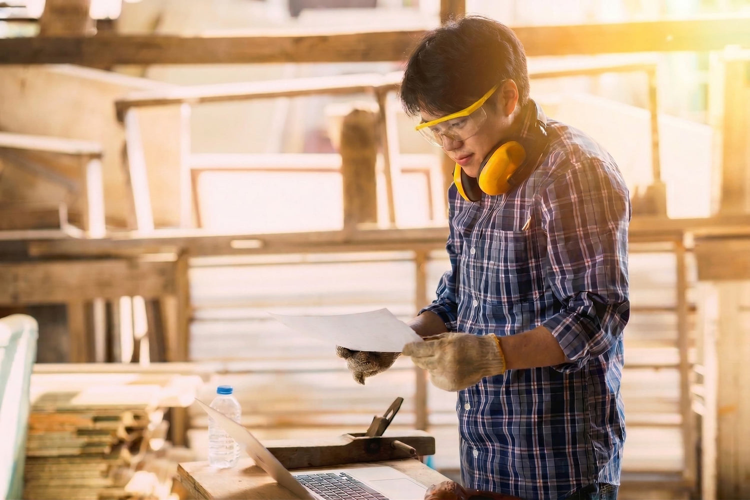 Man working with wood in a workshop wearing safety goggles and ear protection.