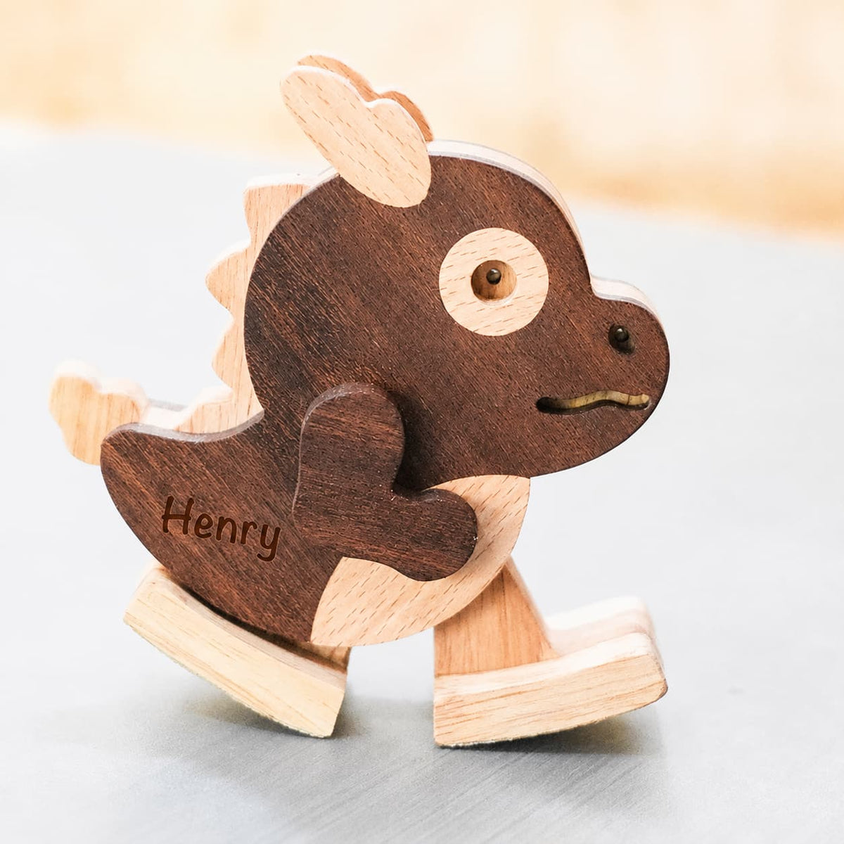 A personalized wooden rocking dragon toy named 'Henry', featuring a dark brown wood body with light natural wood accents, shown on a neutral gray surface.