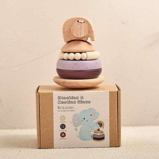 A wooden stacking toy set with a small elephant on top of stacked rings and beads, displayed on top of its printed cardboard box against a plain light beige background.