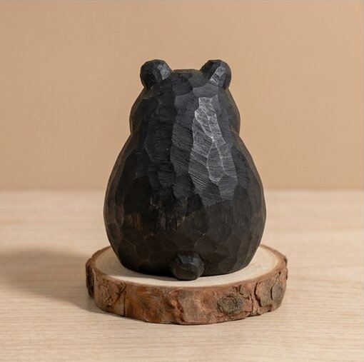Black stone bear sculpture on a wooden base against a beige background
