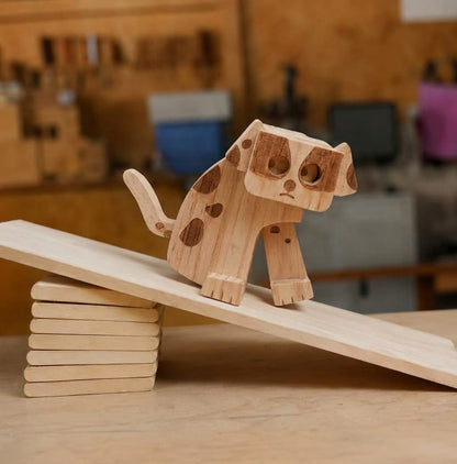 Handmade wooden puppy ramp walker toy with dark walnut spotted patches and large hollow eyes, walking down a mechanical gravity-powered ramp in a carpentry workshop.