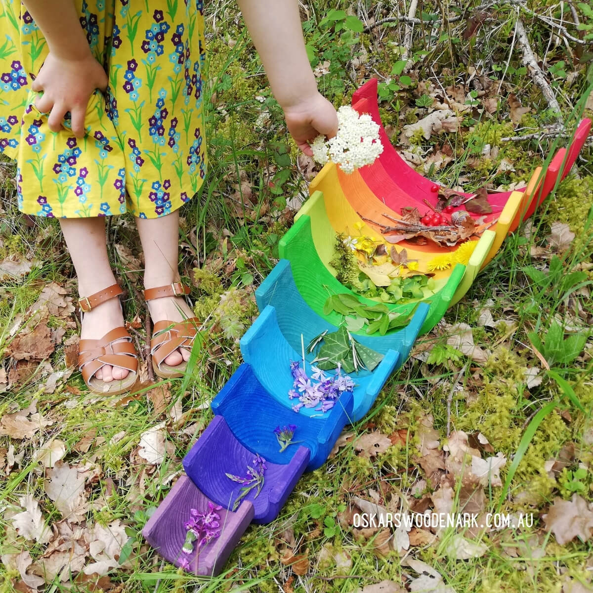 Child playing with a colorful rainbow-shaped toy in a natural setting