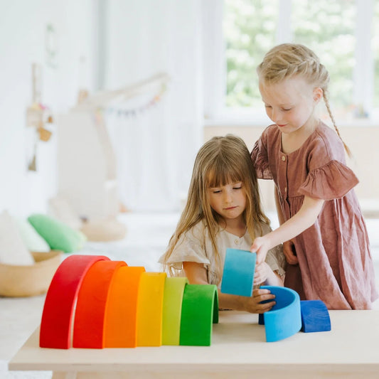 Two young girls playing with colorful building blocks on a table.