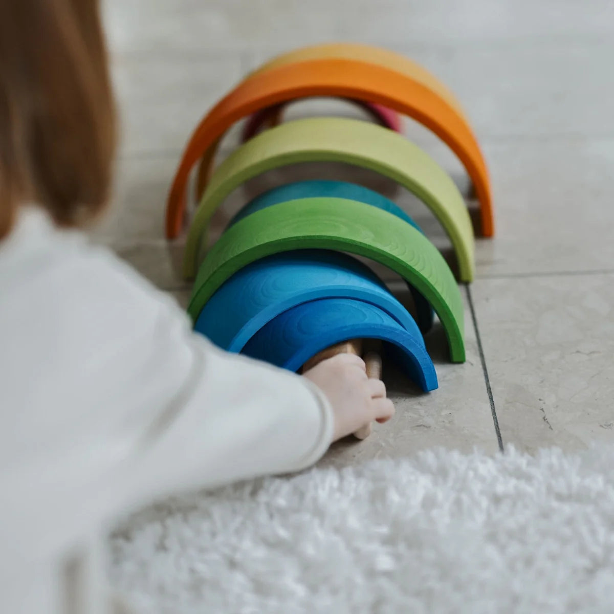 Child playing with colorful wooden rings on a light-colored floor.