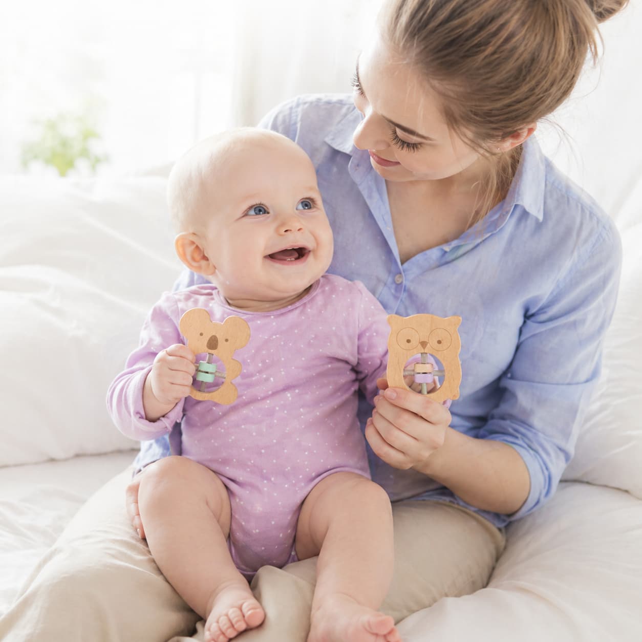 A mother and baby bonding while playing with koala and owl-shaped wooden rattles, featuring an easy-to-grip design for Montessori sensory exploration and early motor skill development.