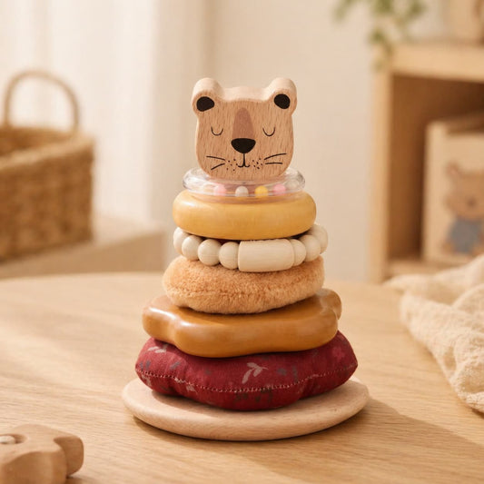 Montessori-inspired wooden bear stacking toy featuring multi-texture sensory rings including plush fabric, natural wood, and a rattle for infant grasping and fine motor skill development.