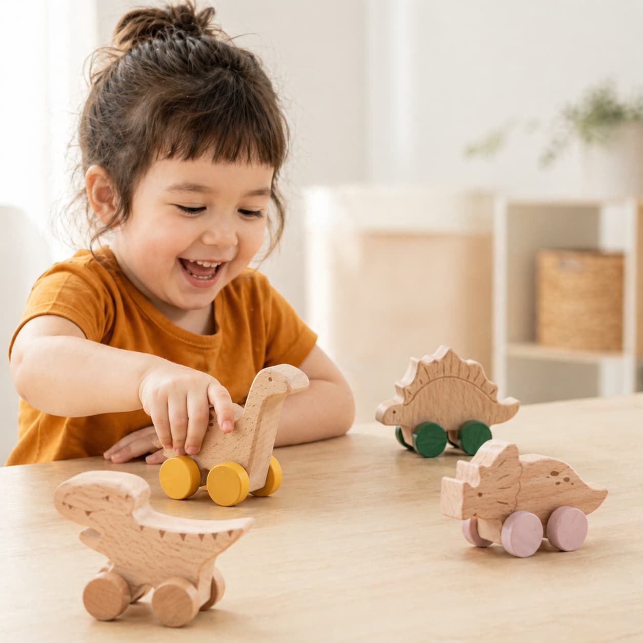 A smiling young girl playing with a set of four Montessori wooden dinosaur push toys on wheels, including a Brachiosaurus, Stegosaurus, T-Rex, and Triceratops, designed to encourage imaginative play and develop fine motor skills in toddlers.