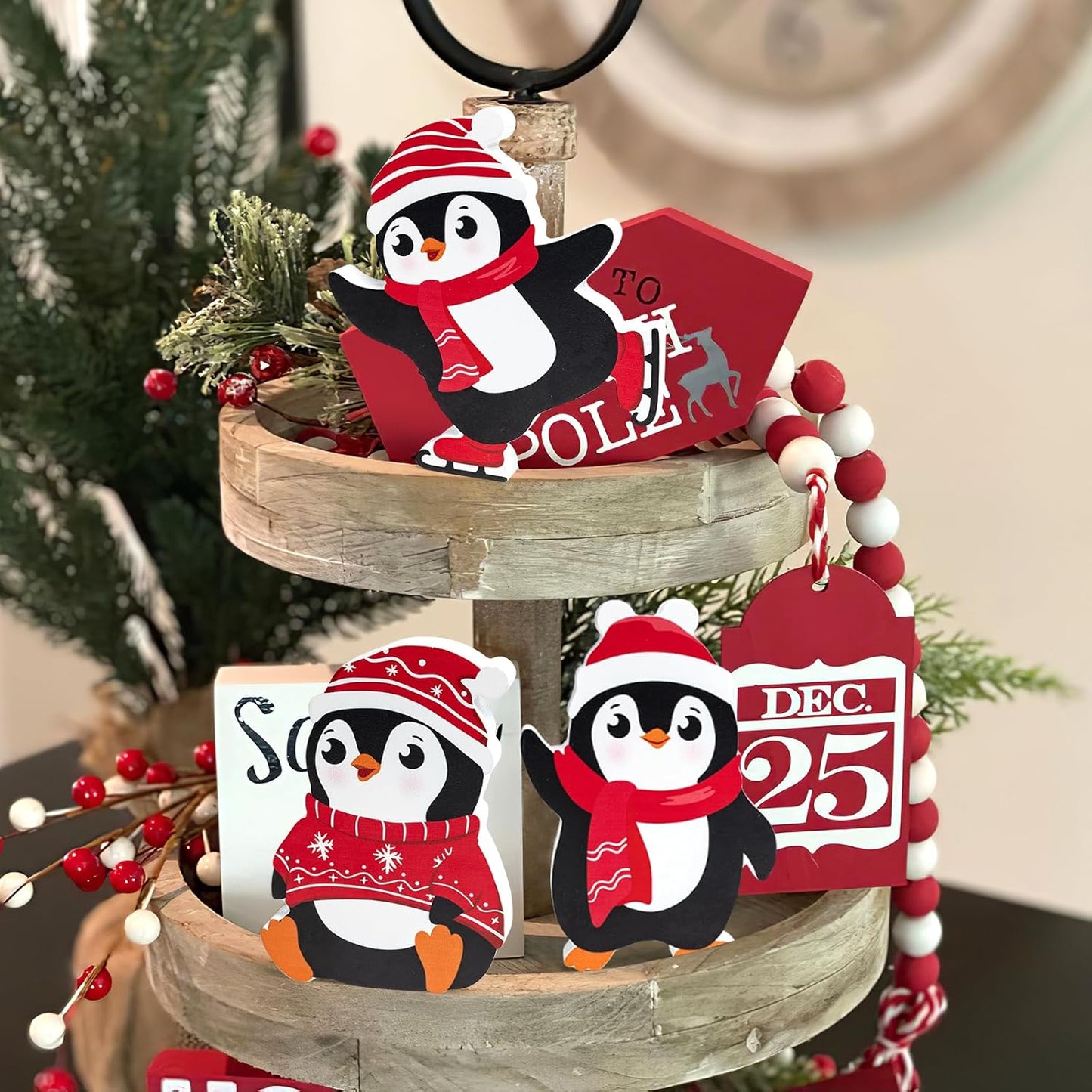 Decorative penguin ornaments with Christmas-themed signs on a tiered wooden stand.