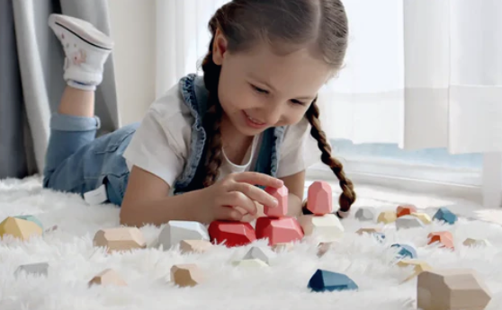 Smiling girl playing with colorful handcrafted Montessori wooden stacking stones on a soft rug