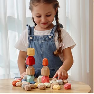 Smiling girl stacking colorful Montessori wooden stones on table, eco-friendly toy