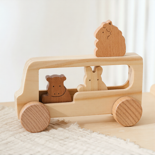 A wooden toy bus with animal characters, made from light natural wood, resting on a textured cream fabric surface.