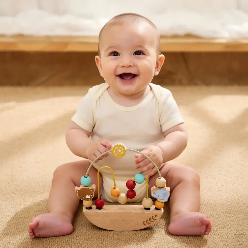Baby sitting on a beige blanket with a wooden toy, smiling.