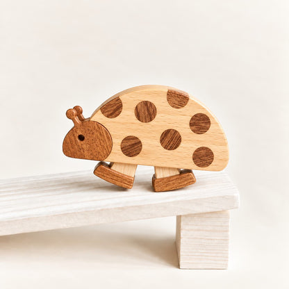 A wooden ladybug ramp walking toy with a light natural wood body and darker brown spots, shown standing on a white wooden platform against a warm off-white background.