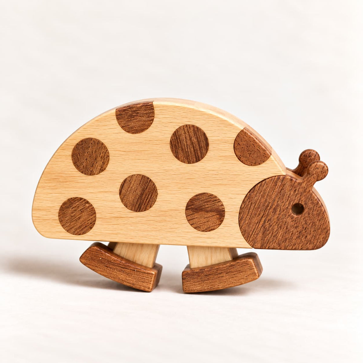 A wooden ladybug toy with a light natural wood body, darker brown spots, and a darker brown head and legs, shown on a clean white background.