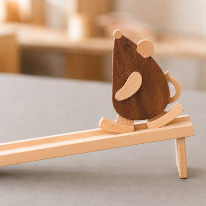 A wooden mouse ramp walker toy made of walnut and beechwood, walking down an inclined wooden track as a mechanical gravity toy.