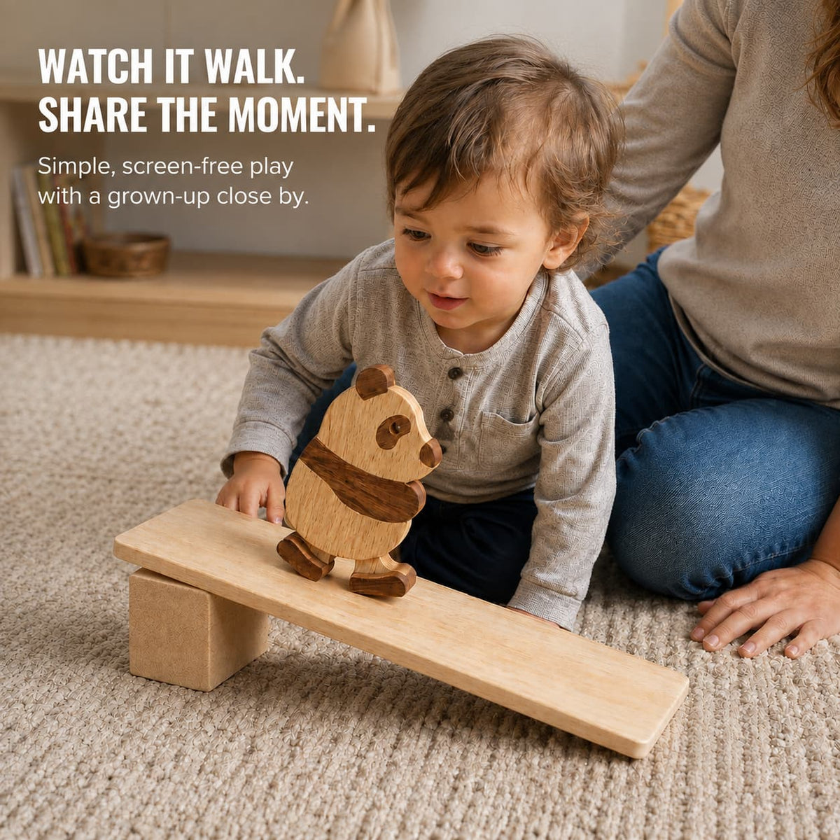 Toddler watching a wooden panda ramp walker move down a wooden ramp with an adult nearby.