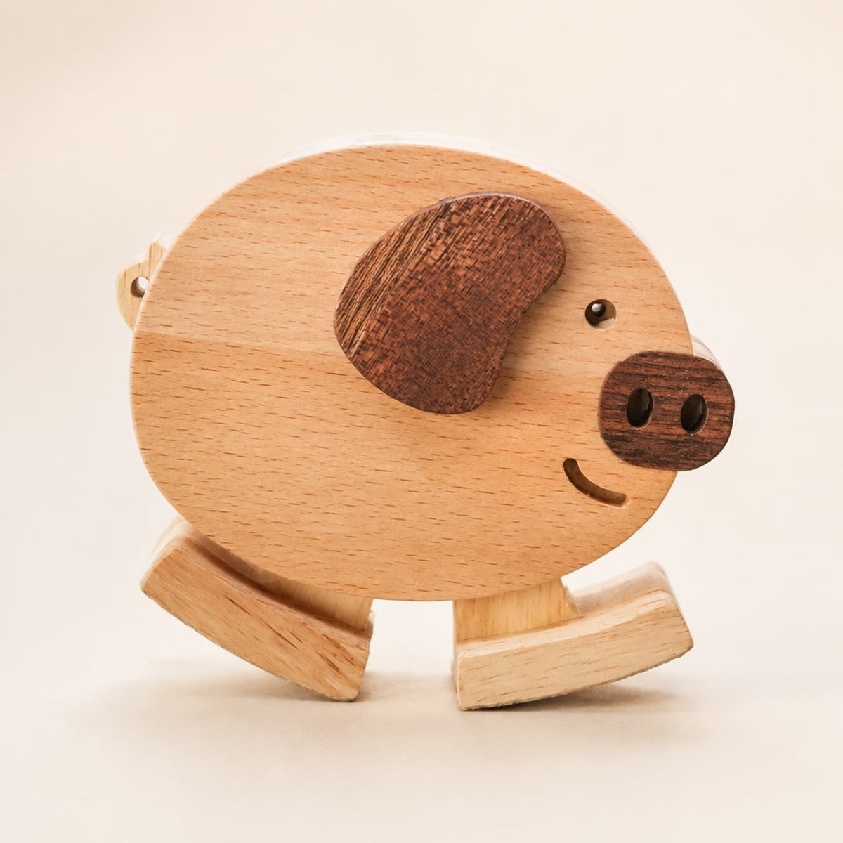 Close-up of a handmade wooden pig ramp walker toy with a dark wood ear, snout and curved walking feet.