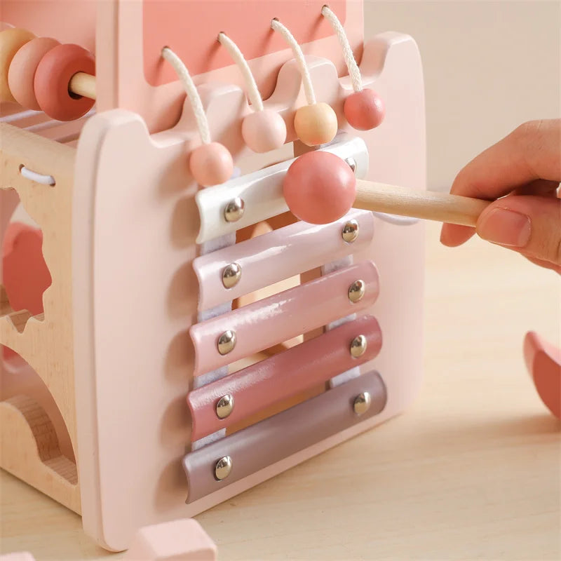 Pink and beige wooden xylophone toy with a hand holding a wooden mallet.